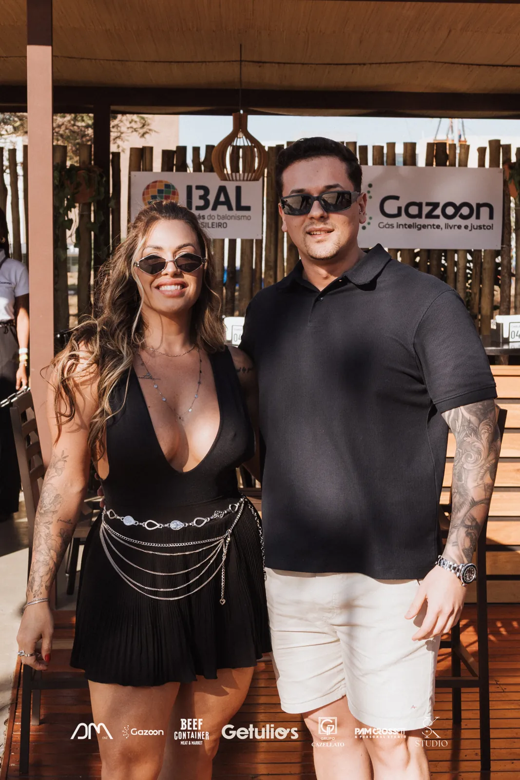 Casal de convidados em evento corporativo com as logos dos patrocinadores no pé da foto